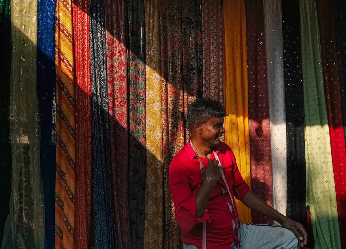 Indian vendor with measuring tape at a vibrant fabric stall in Kolkata, India.