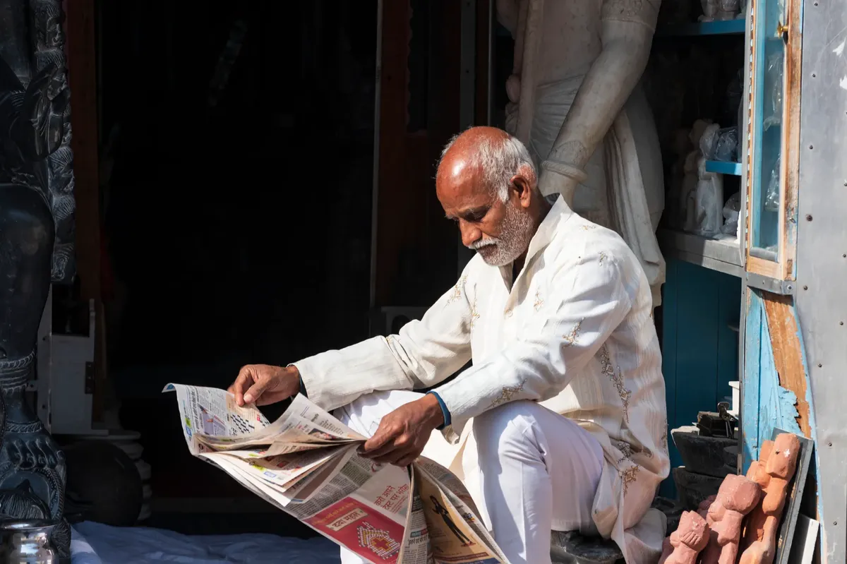 Elderly man in traditional attire reading a newspaper outside in Jaipur, India.
