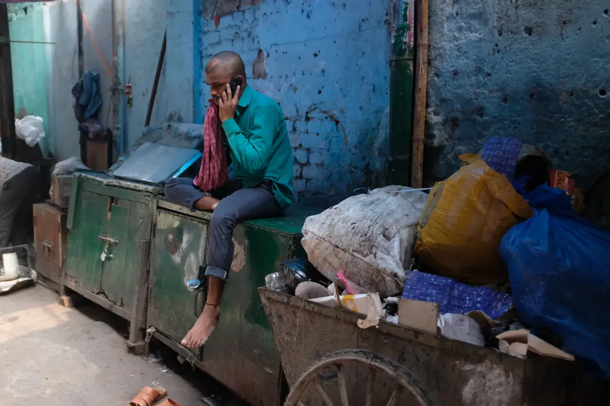 男が、都市スラムの中でスマートフォンを手に持ち、ゴミと廃墟の中にある、インドのニューデリーで。