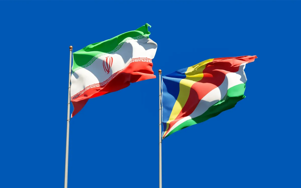 イランとセイシェルズの国家旗が棒に立てられており、明るい青い天気の中で振られている。これは国際関係の象徴である。