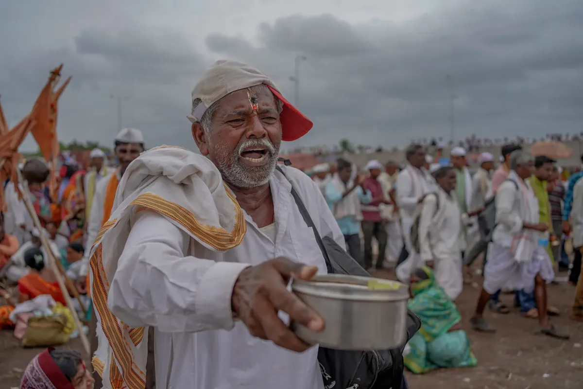 An elderly Indian man in traditional attire seeking alms at a crowded festival in Pandharpur, India.